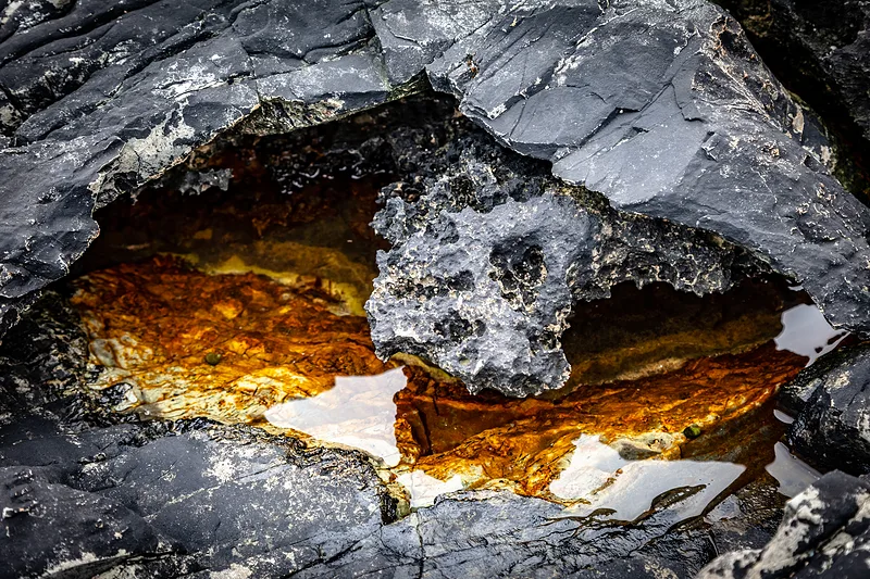 Wasseransammlung zwischen dunklen Felsen mit intensiv orangefarbenen und goldenen Reflexionen.