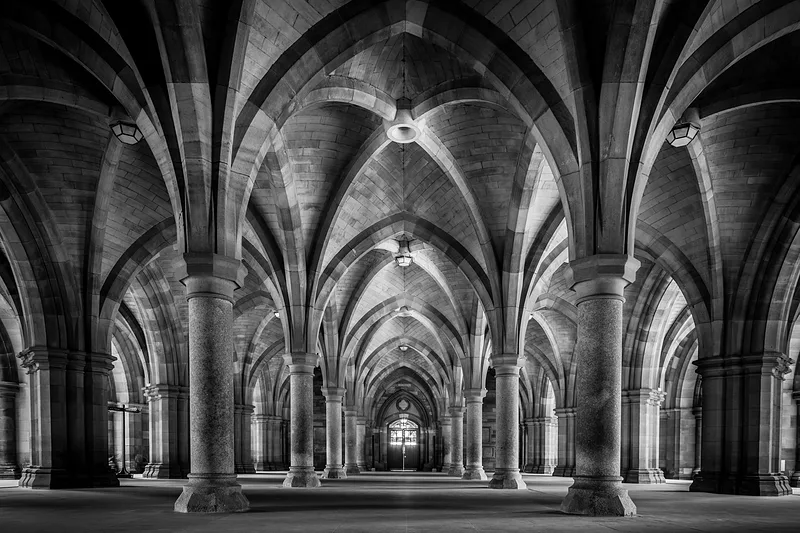 Symmetrische schwarz-weiße Ansicht der Gewölbe und Säulen der Universität Glasgow.